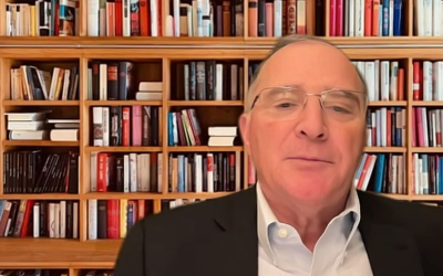 A man in glasses is standing in front of a bookshelf, reflecting on human rights.