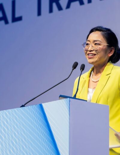 A woman in a yellow jacket standing at a podium speaks passionately about global peace convention.