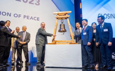 A group of people standing next to a bell on a Global Peace Convention stage.