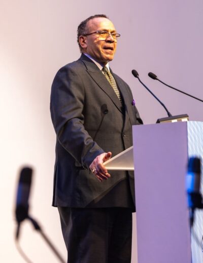 A man in a suit standing at a podium, addressing the Global Peace Convention.