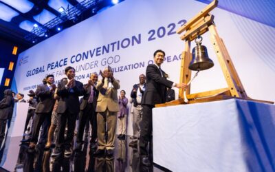 A group of people standing in front of a bell, symbolizing the vision for a Civilization of Peace and National Transformation.