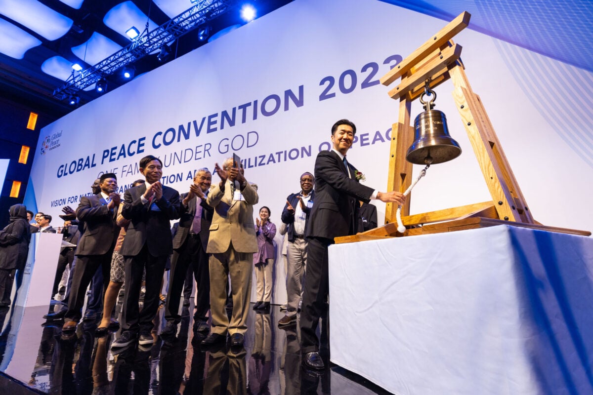 A group of people standing in front of a bell, symbolizing the vision for a Civilization of Peace and National Transformation.