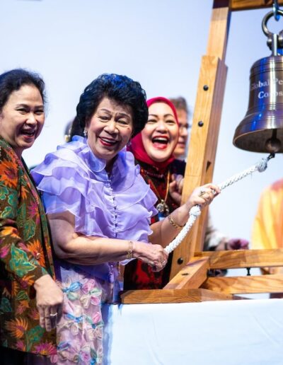 A group of people standing around a wooden bell at the Global Peace Convention.