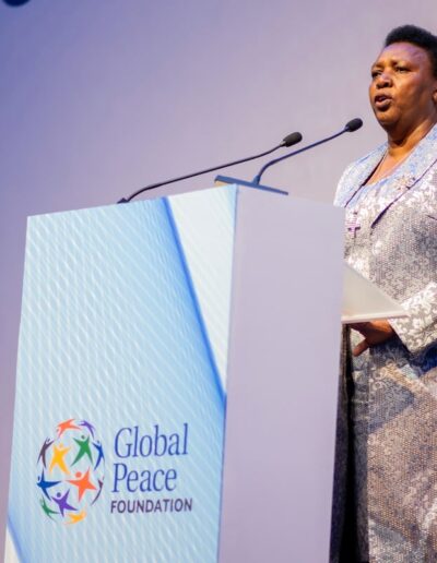 A woman giving a speech at the Global Peace Convention, standing confidently behind a podium.