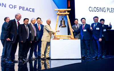 A group of people standing next to a wooden bell, engaged in an animated discussion.