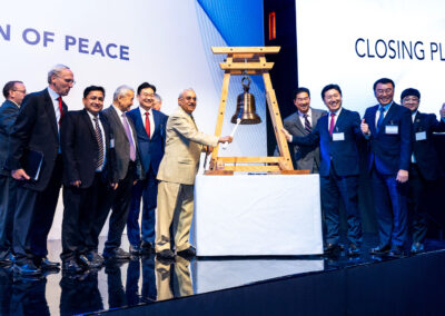 A group of people standing next to a wooden bell, engaged in an animated discussion.